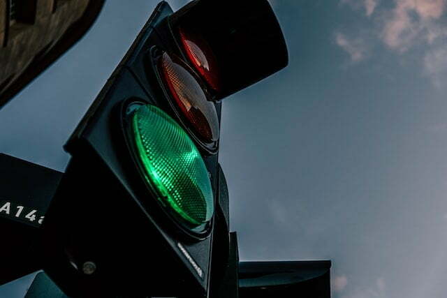 A picture from below of a black traffic light. The green looks to be more illuminated than the orange and red.